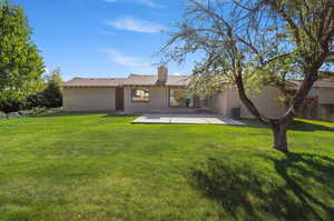 Rear view of property featuring brick siding, a yard, a chimney, and a patio