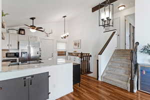 Kitchen with light stone counters, stainless steel appliances, white cabinetry, dark wood-type flooring, and a chandelier