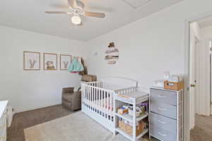 Bedroom with carpet floors, a ceiling fan, and a crib