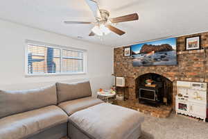 Carpeted living area with a wood stove, ceiling fan, a textured ceiling, and brick wall