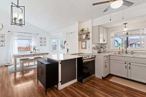 Kitchen featuring stainless steel electric range, a peninsula, plenty of natural light, dark wood-style floors, and vaulted ceiling