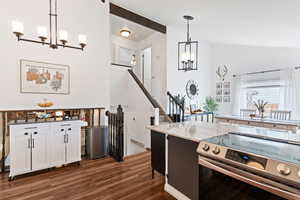 Kitchen featuring suspended lighting, stainless steel electric range, dark wood-type flooring, light stone counters, and lofted ceiling with beams