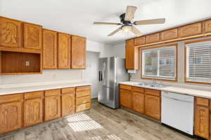 Kitchen with light countertops, stainless steel refrigerator with ice dispenser, dishwasher, a ceiling fan, and wood finish cabinetry