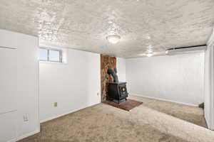 Basement with a wood stove, carpet, and a textured ceiling