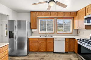 Kitchen with stainless steel appliances, light countertops, a ceiling fan, light wood-style flooring, and wood finish cabinets