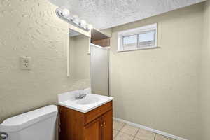 Bathroom featuring a textured wall, vanity, a textured ceiling, a shower stall, and light tile patterned floors