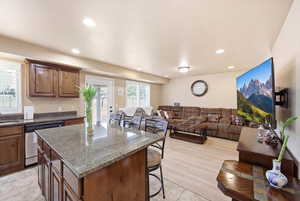 Kitchen featuring open floor plan, a kitchen breakfast bar, dishwasher, a center island, and dark stone countertops