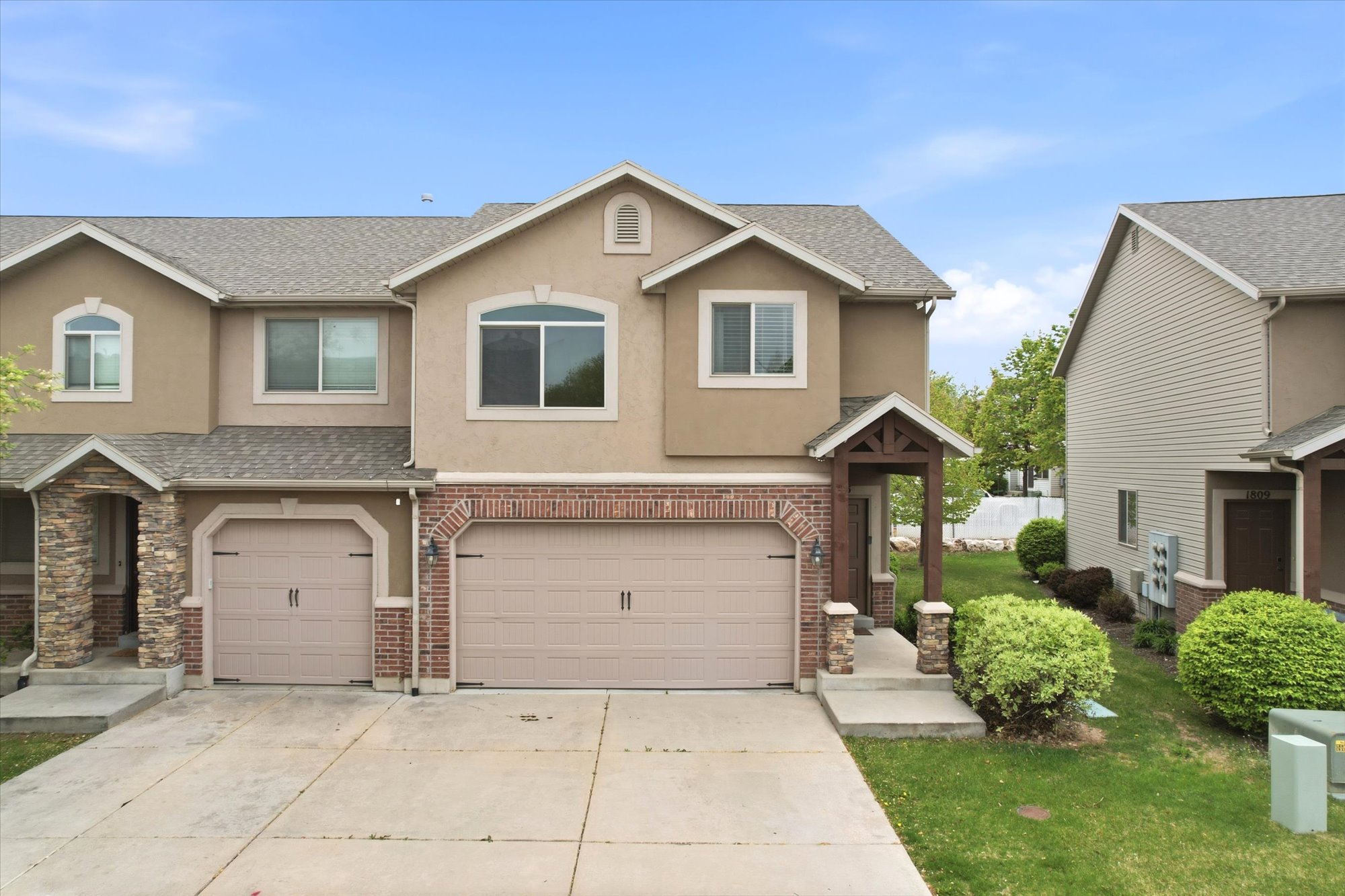 Traditional-style house with stucco siding, a garage, a shingled roof, driveway, and brick siding
