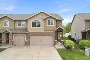 Traditional-style house with stucco siding, a garage, a shingled roof, driveway, and brick siding