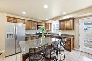 Kitchen featuring stainless steel appliances, a breakfast bar area, dark stone counters, wood finish cabinets, and recessed lighting