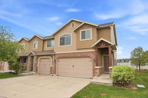 View of front of property featuring a garage, stucco siding, driveway, and brick siding
