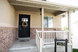 Property entrance featuring a porch, brick siding, and stucco siding