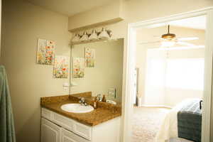 Ensuite bathroom with vanity, light colored carpet, and ceiling fan