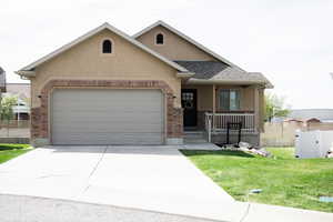 View of front facade featuring an attached garage, driveway, brick siding, a porch, and stucco siding