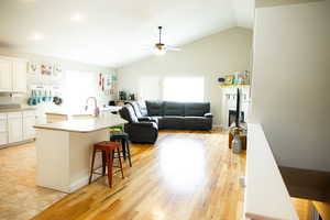Kitchen featuring a center island with sink, a ceiling fan, open floor plan, a breakfast bar area, and white cabinetry