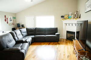 Living room featuring light wood finished floors, a stone fireplace, vaulted ceiling, and a ceiling fan