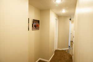 Hallway featuring dark colored carpet and a textured ceiling