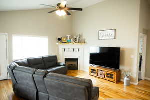 Living area with light wood-style floors, vaulted ceiling, ceiling fan, and a fireplace