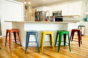 Kitchen featuring light wood finished floors, stainless steel appliances, a breakfast bar area, white cabinets, and recessed lighting