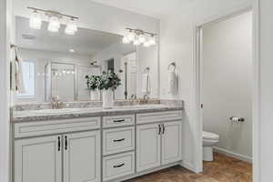 Full bath with double vanity, a stall shower, and stone finish flooring