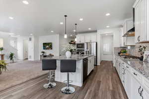 Kitchen with open floor plan, pendant lighting, white cabinetry, a kitchen breakfast bar, and light stone counters