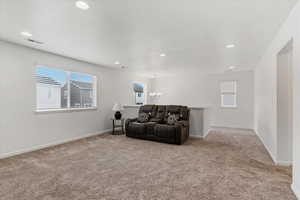 Living area featuring healthy amount of natural light, light carpet, and suspended lighting