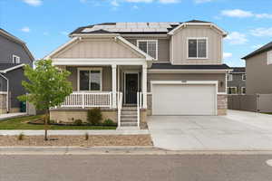 Craftsman-style home featuring board and batten siding, covered porch, solar panels, a garage, and driveway