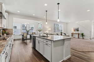 Kitchen featuring white cabinets, open floor plan, light stone countertops, dark wood finished floors, and a center island with sink