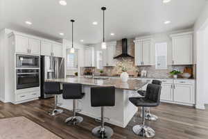 Kitchen featuring stainless steel appliances, light stone counters, a kitchen island with sink, white cabinetry, and a breakfast bar