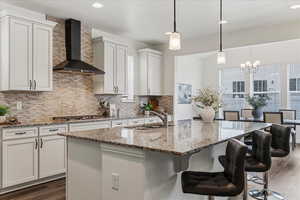 Kitchen featuring light stone countertops, dark wood-style flooring, an island with sink, backsplash, and white cabinets