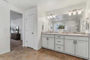 Bathroom with double vanity, a stall shower, and stone finish flooring