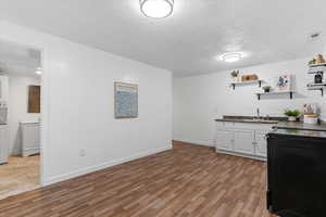 Bar featuring dark countertops, white cabinets, open shelves, light wood-type flooring, and stacked washer / dryer