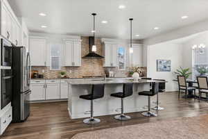 Kitchen with light stone counters, a center island with sink, white cabinetry, a breakfast bar, and healthy amount of natural light