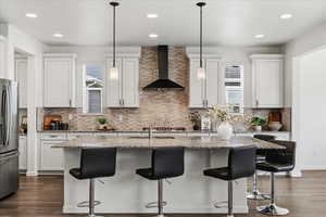 Kitchen with light stone counters, a kitchen island with sink, dark wood finished floors, stainless steel fridge, and decorative light fixtures