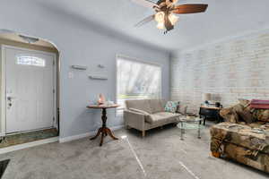 Carpeted living room with arched walkways, plenty of natural light, ceiling fan, and a textured ceiling
