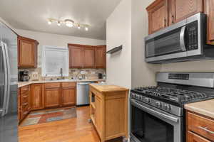 Kitchen featuring stainless steel appliances, light countertops, wood finish cabinets, decorative backsplash, and light wood-type flooring