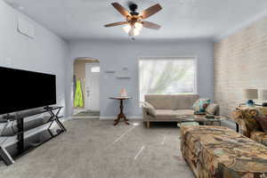 Carpeted living area with arched walkways, a textured ceiling, and ceiling fan
