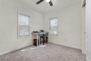 Carpeted office space with a ceiling fan and baseboards