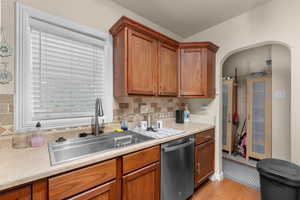 Kitchen with light countertops, dishwasher, wood finish cabinets, light wood-style flooring, and decorative backsplash