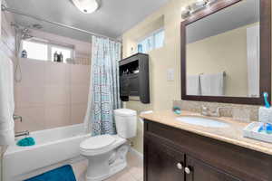 Full bath with a textured wall, vanity, shower / bath combo with shower curtain, light tile patterned floors, and a textured ceiling