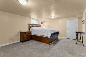 Bedroom featuring a textured ceiling, light colored carpet, and a textured wall