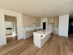 Kitchen with a kitchen bar, an island with sink, light wood-type flooring, and cream cabinets
