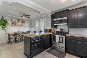 Kitchen with stainless steel appliances, dark cabinetry, crown molding, a peninsula, and light wood-type flooring