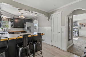Kitchen with a breakfast bar area, stainless steel appliances, dark cabinetry, ornamental molding, and a wainscoted wall