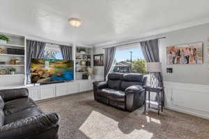 Living room featuring carpet flooring, healthy amount of natural light, a decorative wall, wainscoting, and a textured ceiling