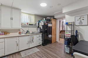 Kitchen featuring black fridge with ice dispenser, light countertops, white cabinets, and light wood finished floors