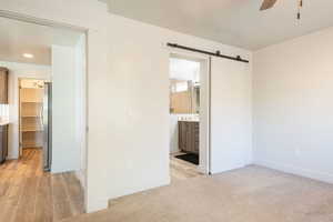 Unfurnished bedroom featuring a spacious closet, a barn door, freestanding refrigerator, ensuite bathroom, and ceiling fan