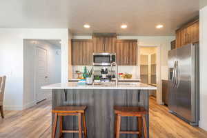 Kitchen featuring wood finish cabinetry, stainless steel appliances, a breakfast bar area, light wood-style flooring, and recessed lighting
