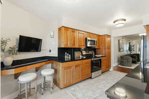 Kitchen featuring stainless steel appliances, dark countertops, wood finish cabinets, and a breakfast bar