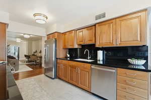 Kitchen with stainless steel appliances, backsplash, a desk, wood finish cabinetry, and dark stone countertops